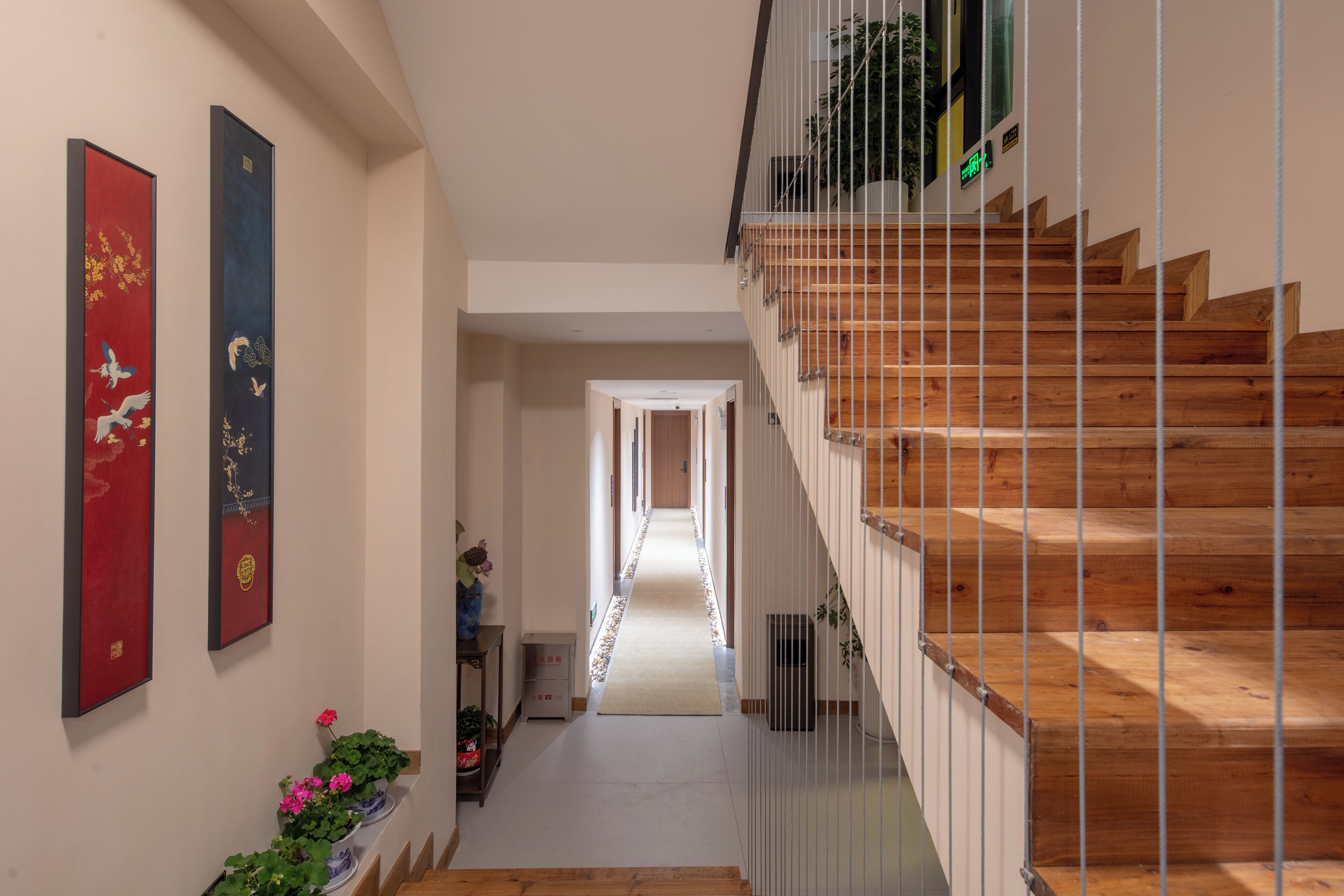 A modern interior with a wooden staircase, a hallway leading to a door, and two framed artworks on the wall.