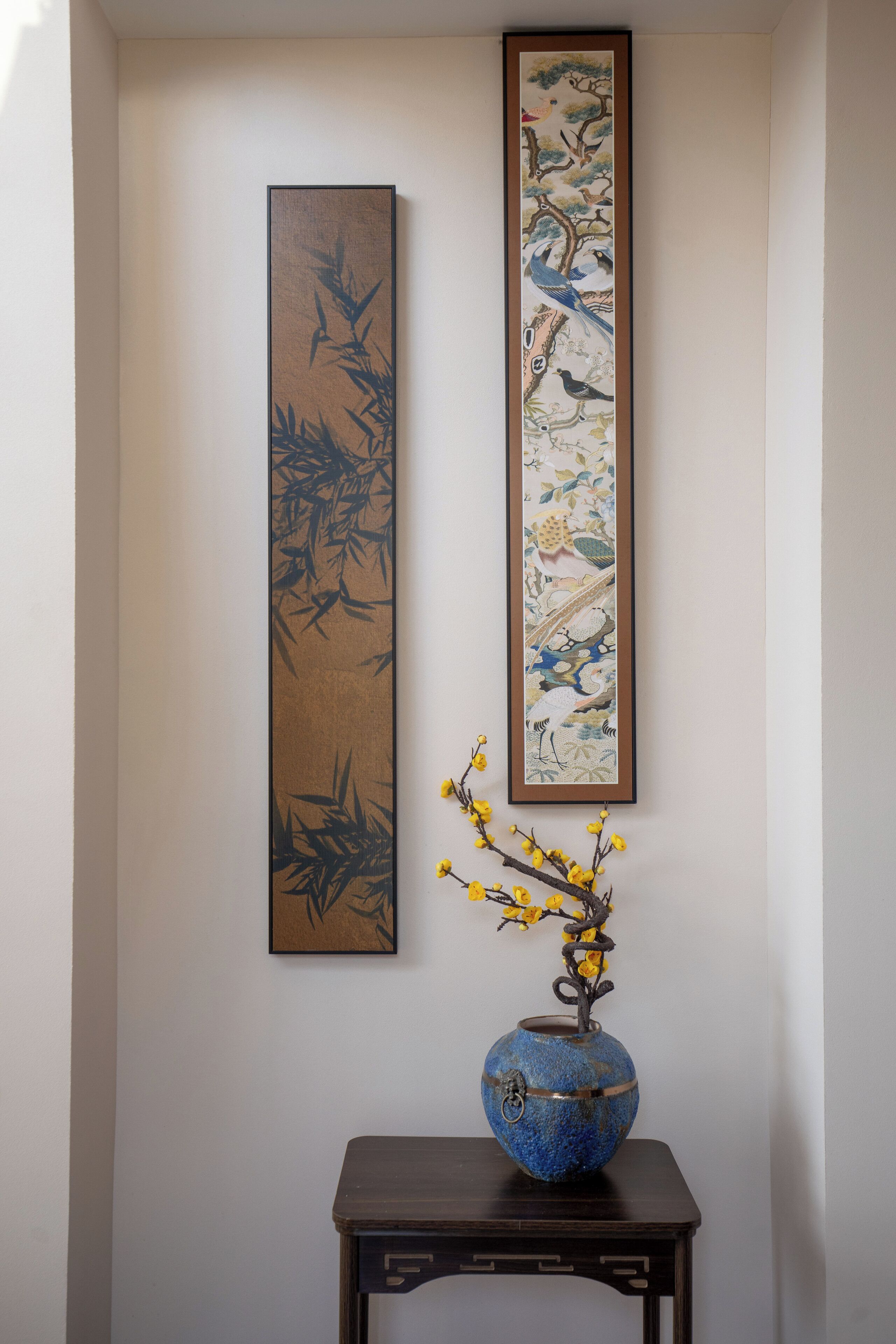 Una pared con dos cuadros enmarcados y un jarrón con flores amarillas sobre una mesa de madera oscura.