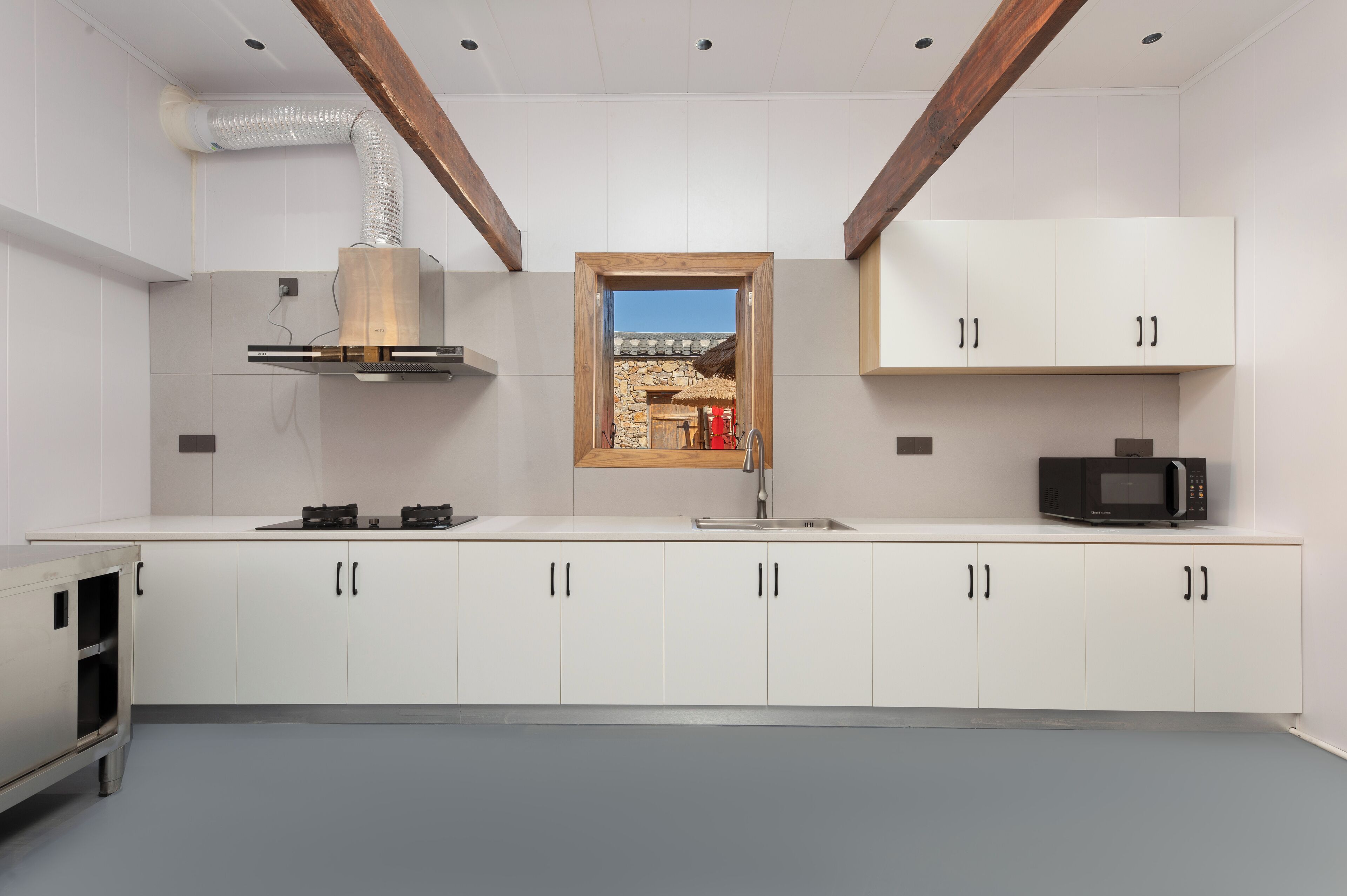 A modern kitchen with white cabinets, a built-in microwave, and a view of a stone building through a window.