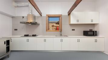 A modern kitchen with white cabinets, a built-in microwave, and a view of a stone building through a window.