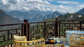 Ein Balkon mit Korbmöbeln, einem Tisch mit Obst und Blick auf Berge.