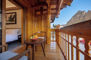 A wooden balcony with a bed, a table with fruit, and a mountain view.