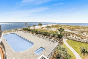 A rooftop pool with a view of the ocean, surrounded by palm trees and a walking path.