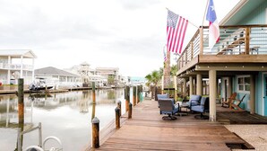A waterfront hotel with a wooden deck, outdoor seating, and flags. - The Boat House:  Key Allegro, Water Front, On Canal! (Rockport)