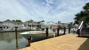 A boat docked at a marina with a wooden deck, a house with a balcony, and a flag. - The Boat House:  Key Allegro, Water Front, On Canal! (Rockport)