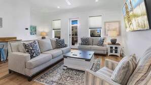 A spacious living room with a large sofa, a coffee table, and a TV mounted on the wall. - Whimsical Way 4 Beds 4 Baths NEW Near Beach (Gulf Shores)