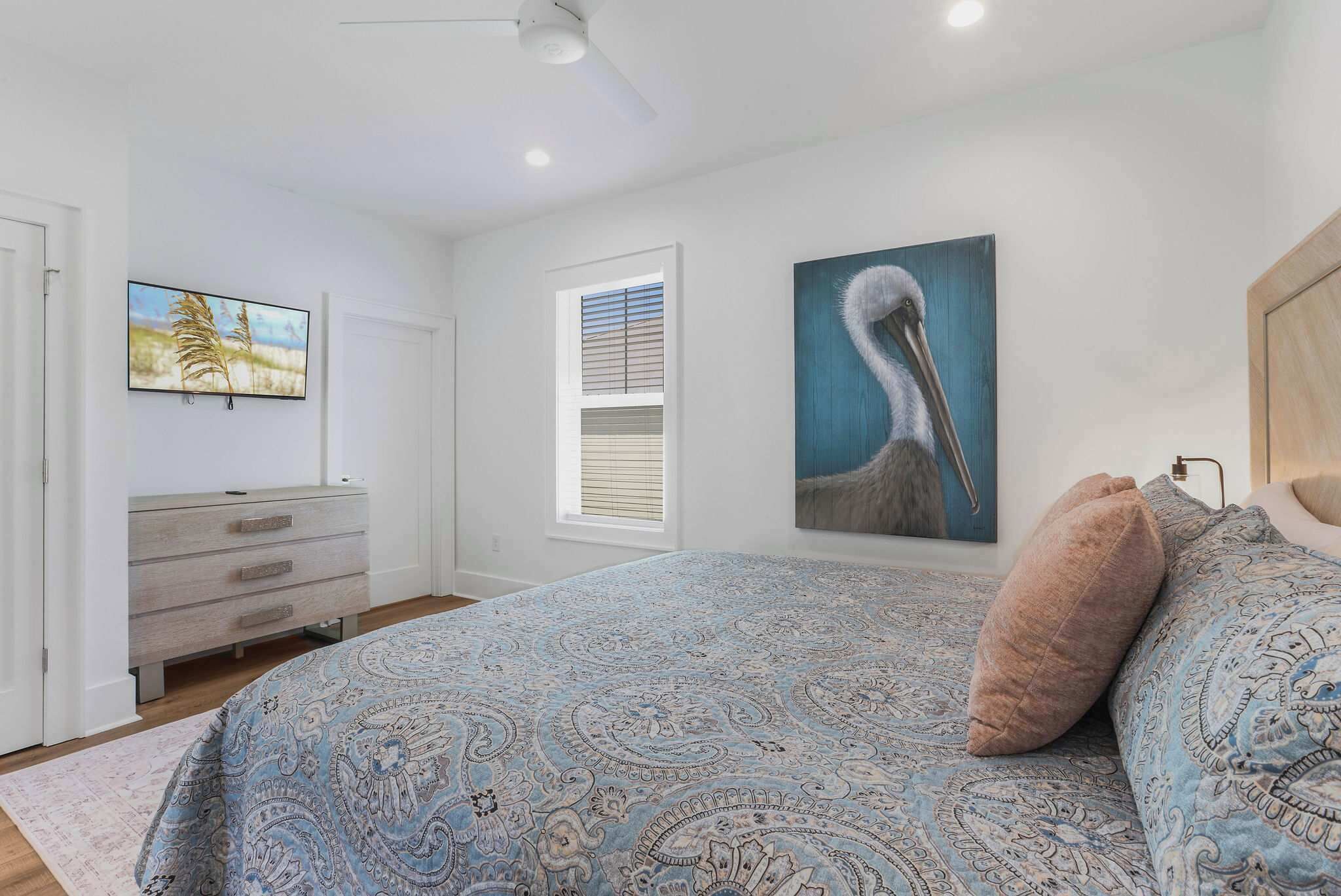 A bedroom with a large bed, a dresser, a window with blinds, and two wall-mounted paintings.