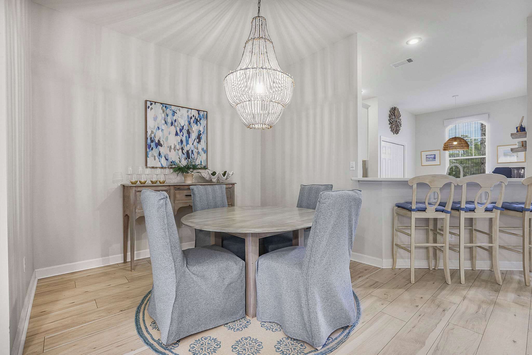 Ein Essbereich mit einem runden Tisch, grau gepolsterten Stühlen, einer Chandelier und einem gemusterten Teppich.
