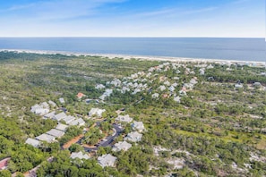 Vue aérienne d’un quartier résidentiel avec des maisons, des routes et une plage en arrière-plan.