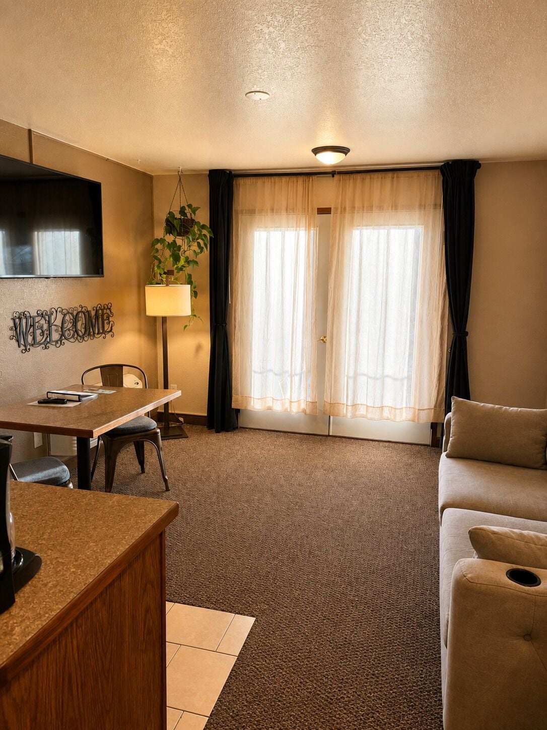 Une chambre d’hôtel comprenant un coin repas, un canapé, une télévision et une fenêtre avec des rideaux.
