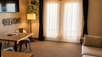 A hotel room with a dining area, a sofa, a TV, and a window with curtains.
