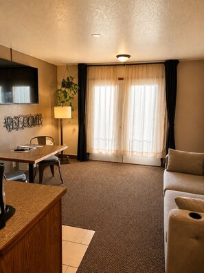 A hotel room with a dining area, a sofa, a TV, and a window with curtains.