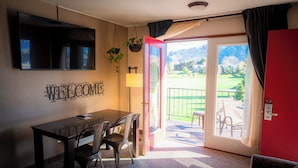 A room with a table and chairs, a TV mounted on the wall, a 'WELCOME' sign, and a door leading to a balcony with a view of a green landscape. - Mountain View Lodge and Resort (Manson)