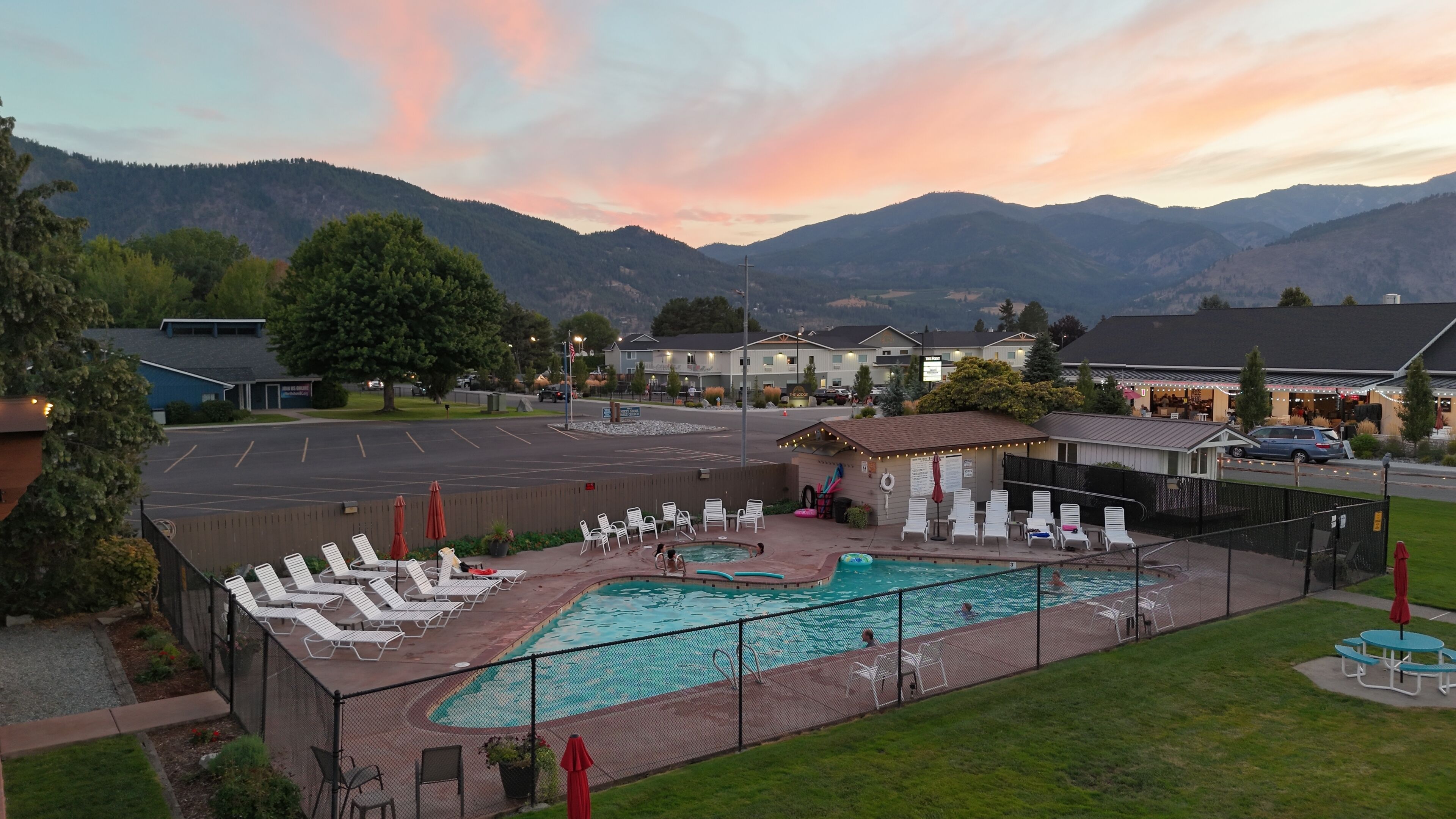 Une piscine dotée de chaises longues et d’un espace de repos couvert, le tout entouré d’une clôture, avec des montagnes en toile de fond.