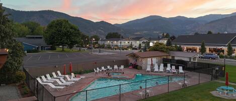 Une piscine dotée de chaises longues et d’un espace de repos couvert, le tout entouré d’une clôture, avec des montagnes en toile de fond.