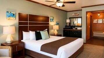 A hotel room with a large bed, bedside lamps, a ceiling fan, artwork on the walls, and a dresser with a mirror.