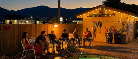Eine Gruppe von Menschen sitzt am Abend in einer beheizten Außenpoolanlage, im Hintergrund Berge.