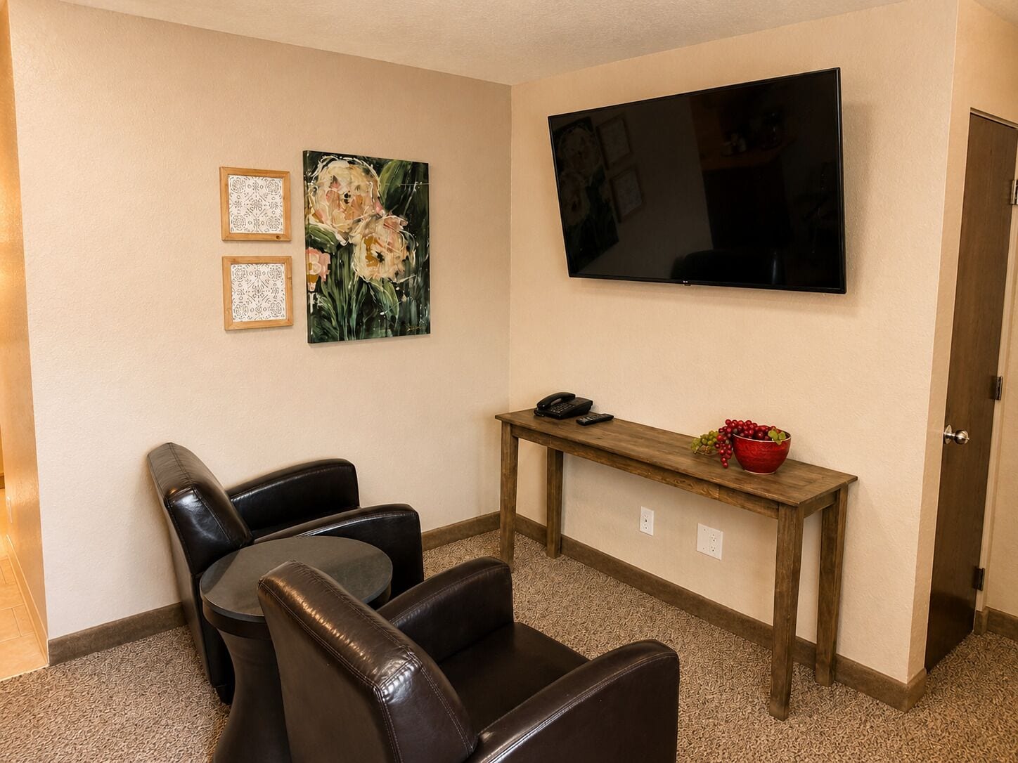 Ein Zimmer mit Fernseher, Schreibtisch mit Telefon und einer Obstschale, sowie zwei Ledersesseln.