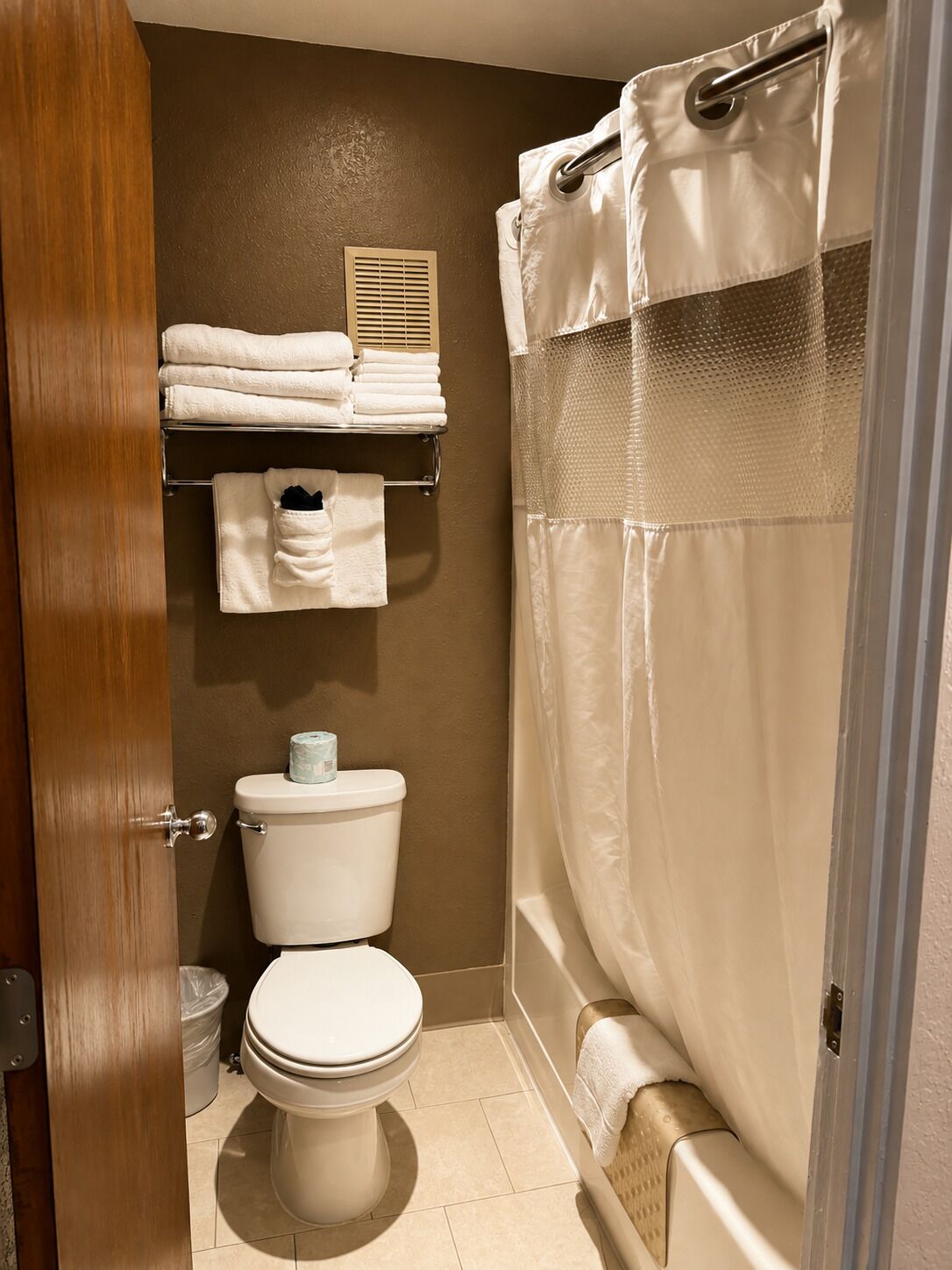 A bathroom with a toilet, a shelf with folded towels, and a shower curtain.