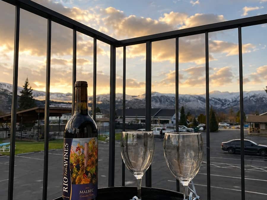 A balcony with a bottle of Malbec wine, two glasses, and a platter of cheese and crackers.