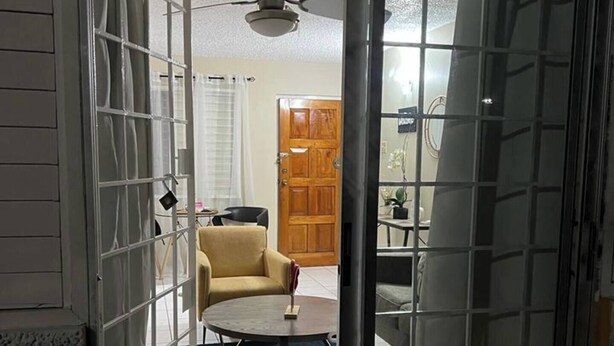 Una habitación con puerta corredera de vidrio que da a una sala de estar con ventilador de techo, una mesa redonda y un sofá.