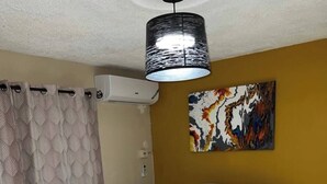 Un dormitorio con una colcha estampada, un aplique de techo, un cuadro en la pared y una ventana con cortinas.