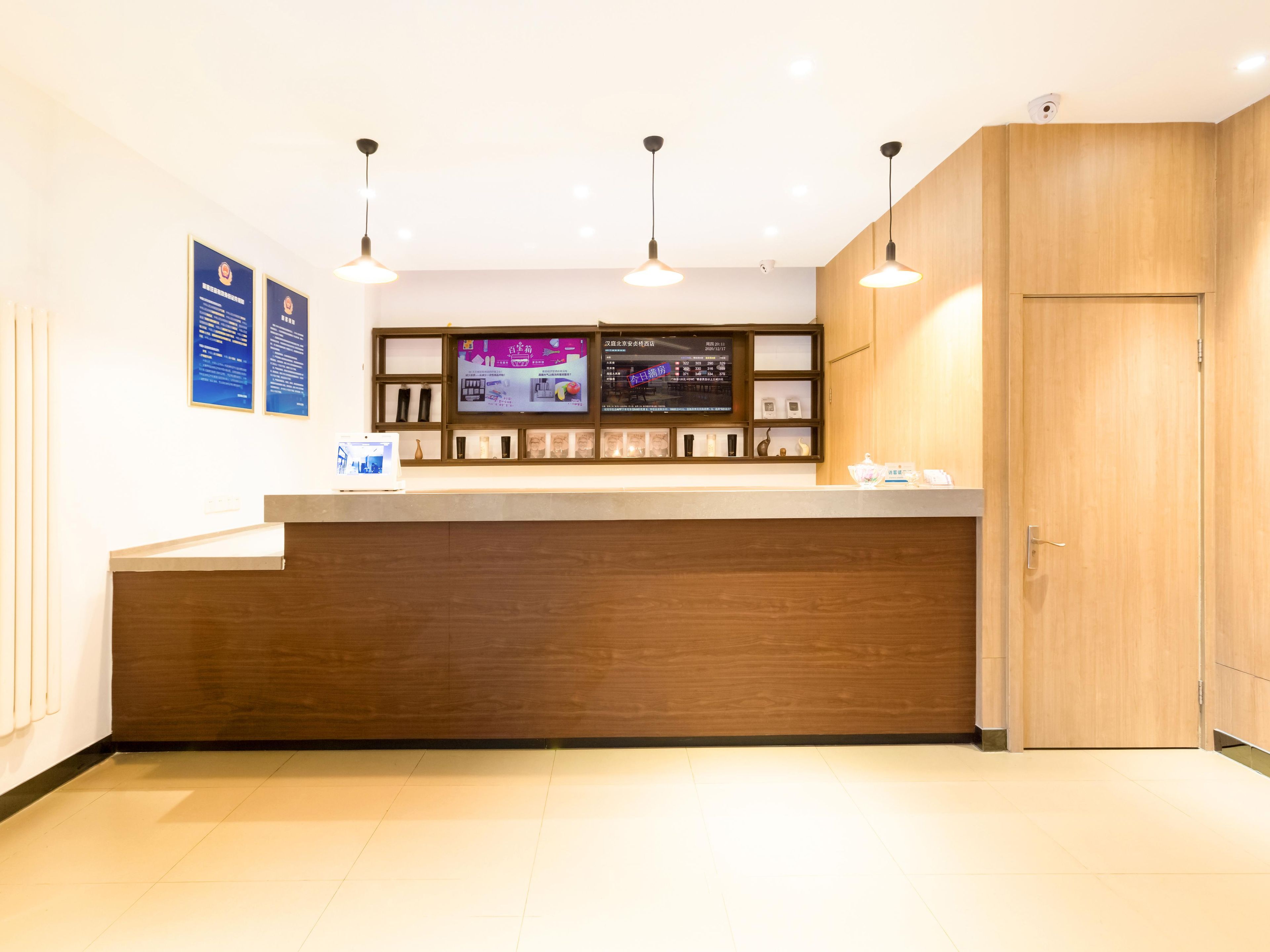 Un mostrador de recepción con encimera de madera, iluminación colgante, una pantalla digital y un armario de madera.