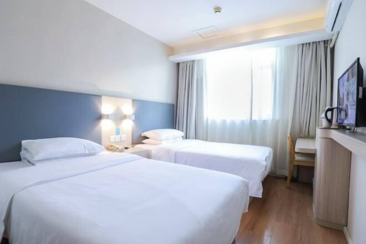 Habitación de hotel con dos camas, un escritorio, una silla, un televisor y una ventana con cortinas.