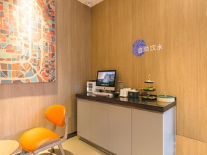 Una taquilla amb un monitor d'ordinador, una taula petita amb un dispensador de begudes i un cartell fixat a la paret.