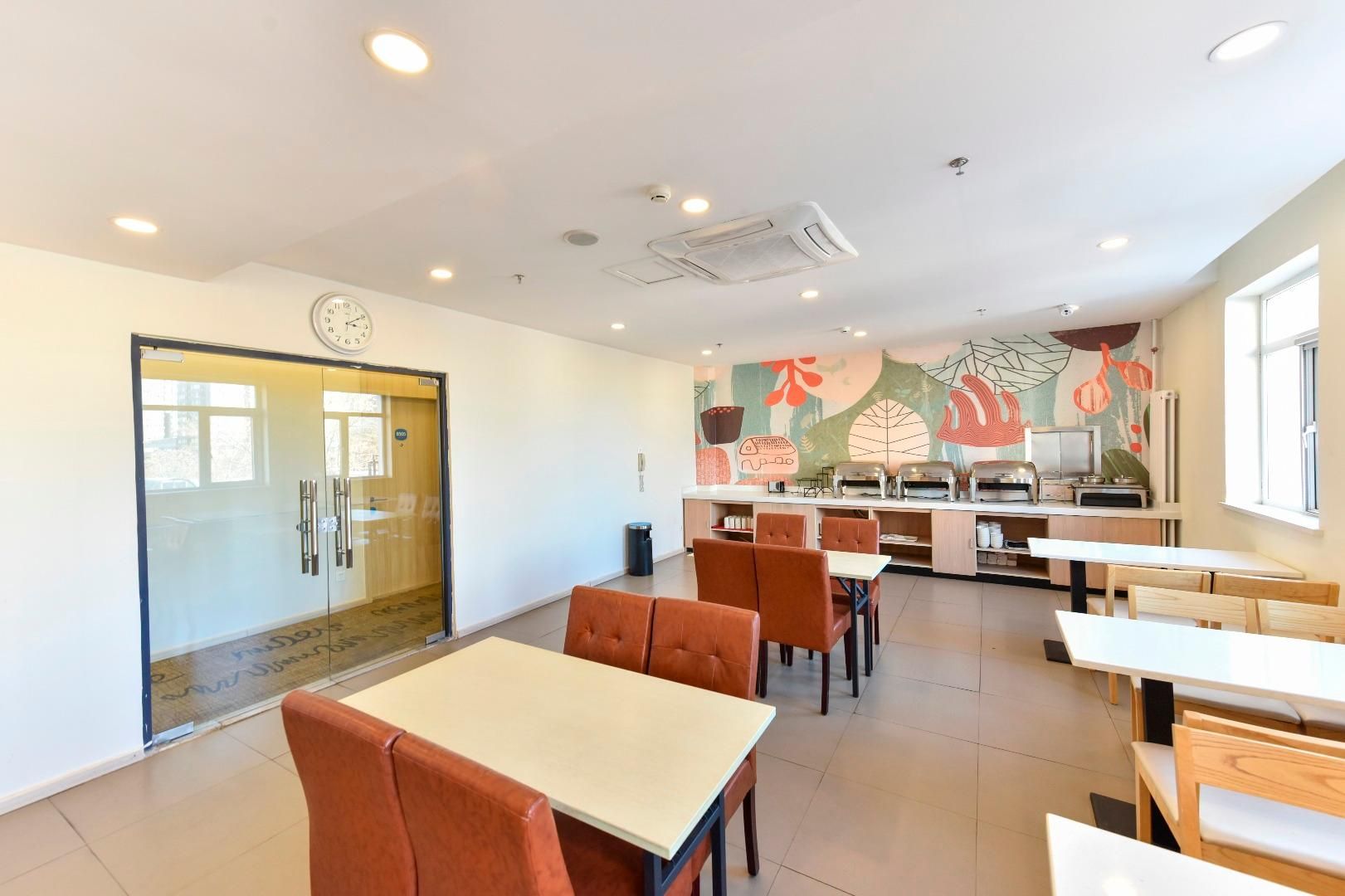 Un espace de repas moderne avec des tables et des chaises, une cuisine en arrière-plan et une horloge au mur.