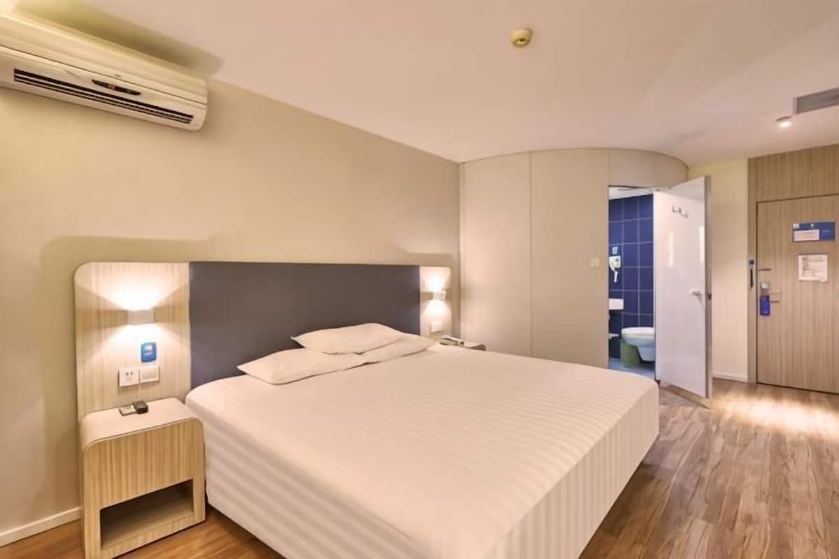 Habitación de hotel con cama, mesita de noche, lámpara y aire acondicionado.