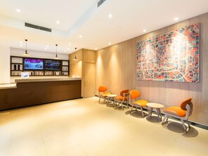 Zona de recepció d'hotel amb taulell de fusta, diverses pantalles i cadires taronges.