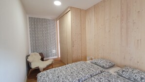 Un dormitorio con un armario de madera, una colcha estampada y un sillón con una manta de piel.