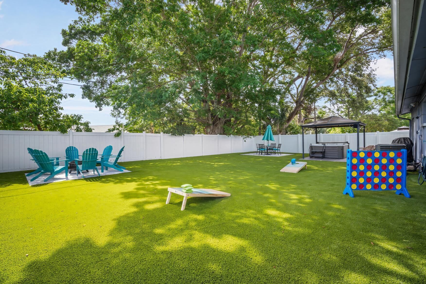 A backyard with artificial grass, a table with chairs, a gazebo, and a game board.