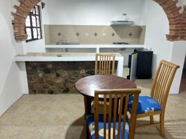 Una cocina compacta con una pared de piedra, una mesa de comedor con sillas y una estufa empotrada.