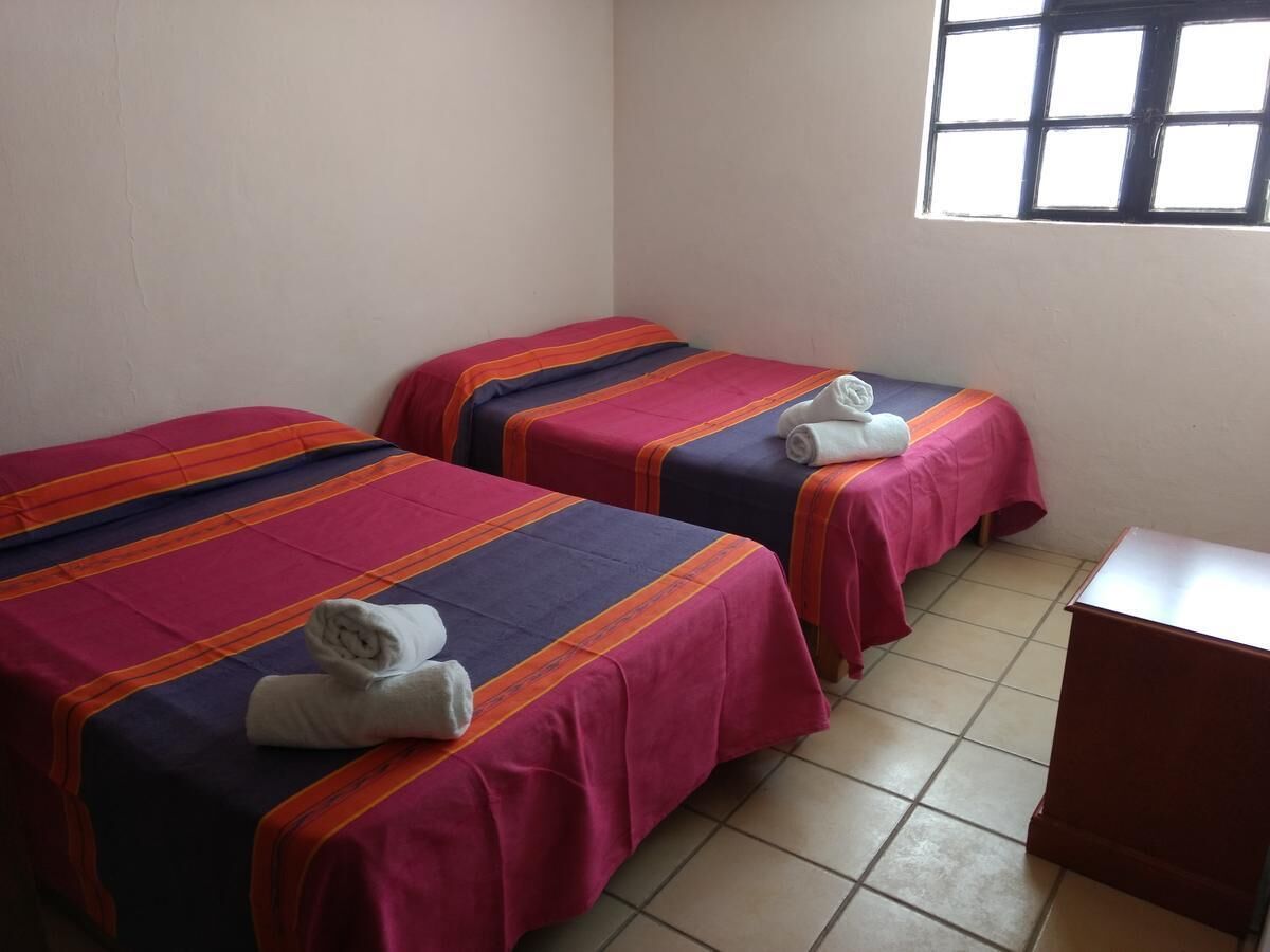 Two single beds with striped bedding and rolled towels, a small wooden desk, and a window with bars.