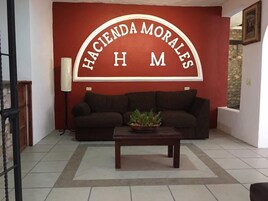 Una sala de estar con una pared roja, un sofá marrón, una mesa de centro de madera y una planta en maceta.