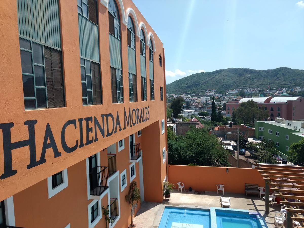 Edificio llamado 'Hacienda Morales' con zona de piscina y vista a un pueblo y colinas al fondo.