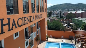 Un bâtiment appelé « Hacienda Morales », doté d’une piscine et offrant une vue sur une ville et des collines en arrière-plan.
