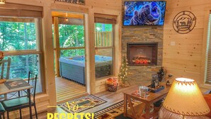 A cozy cabin interior with a fireplace, a TV mounted on the wall, and a wooden sign above the fireplace.