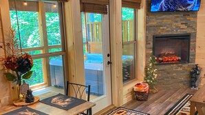 A cozy cabin interior with a fireplace, a television mounted on the wall, and a dining area with a view of the outdoors.