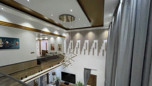 A spacious living area with a high ceiling, a staircase, and a large flat-screen TV. - Golden Breeze Villa, Luxury 5-bedroom Villa with Private Pool (Accra)