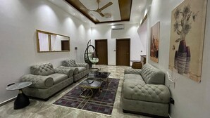 A modern living room with two sofas, a coffee table, and a hanging chair. There is a ceiling fan, a mirror, and a painting on the wall. - Golden Breeze Villa, Luxury 5-bedroom Villa with Private Pool (Accra)