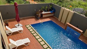 A rooftop swimming pool with white lounge chairs, a small waterfall feature, and potted plants. - Golden Breeze Villa, Luxury 5-bedroom Villa with Private Pool (Accra)