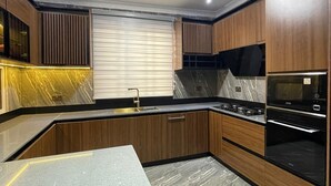 A modern kitchen with wooden cabinets, a marble countertop, and built-in appliances. - Golden Breeze Villa, Luxury 5-bedroom Villa with Private Pool (Accra)
