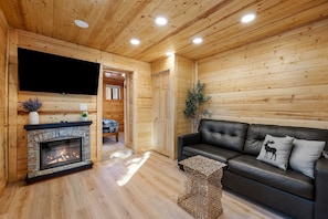 A wooden interior with a fireplace, leather sofa, and a television.