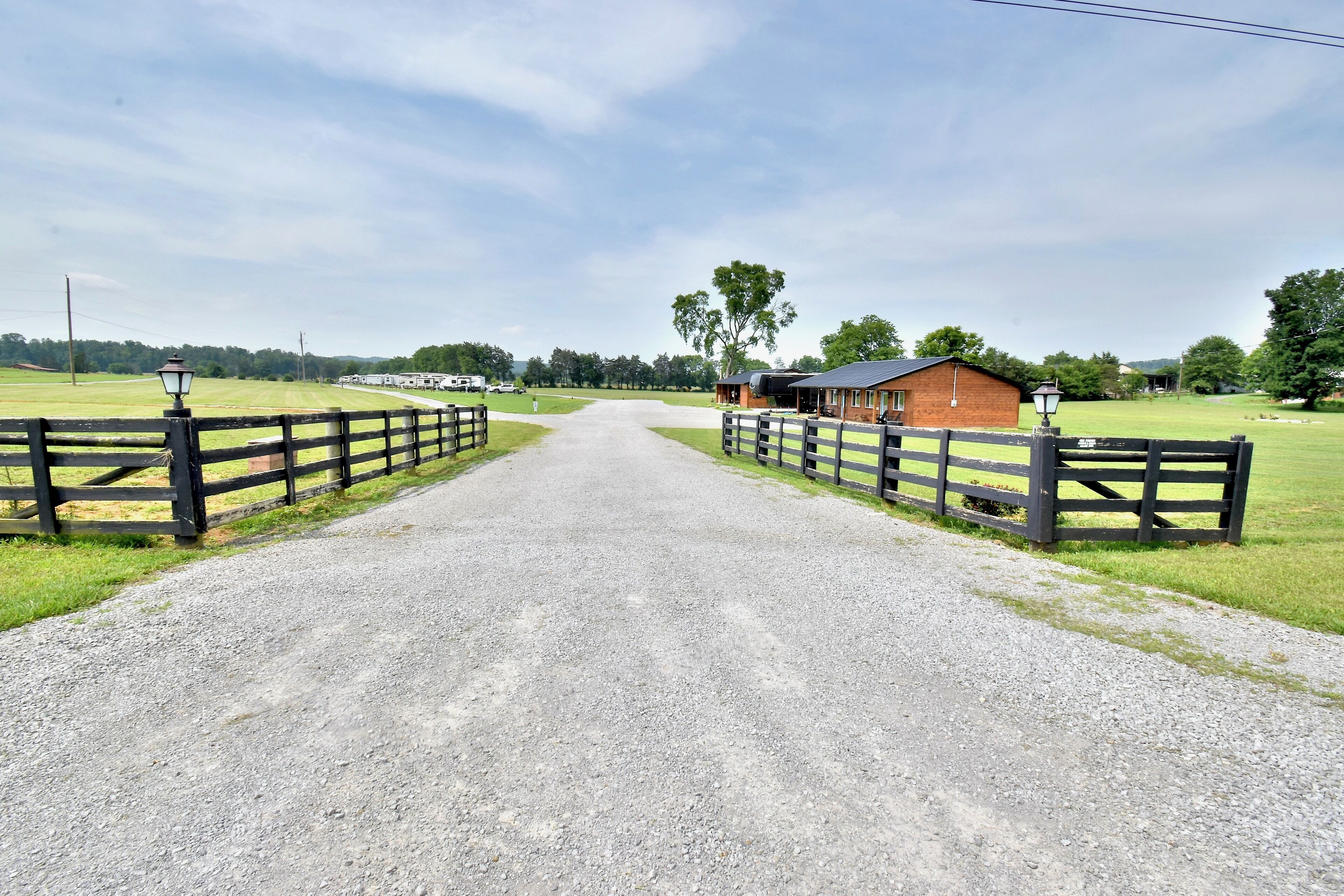 A gravel road leading to a farm with a wooden fence and a small brick building.