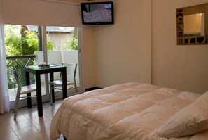 Une chambre avec un lit, un téléviseur fixé au mur, une table avec des chaises et une porte-fenêtre coulissante donnant sur un balcon.