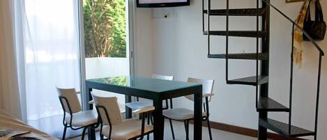 A dining area with a table and chairs, a television mounted on the wall, and a spiral staircase.