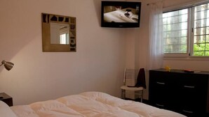 Ein Schlafzimmer mit einem Bett, einem an der Wand befestigten Fernseher, einem Sessel und einer Kommode.